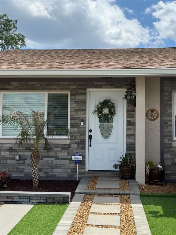 A white front door with a wreath sits on a stone-faced exterior with pavers — 2710 CHARING CROSS WAY, ORLANDO, FL