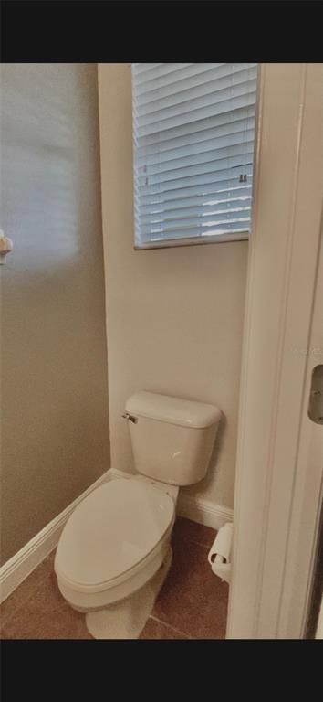 A small bathroom features a white toilet, tiled flooring, and a window with white blinds — 4956 LUGE LANE, ORLANDO, FL