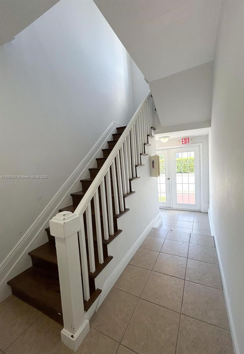 A staircase with dark wood treads and white railings leads upward in a tiled hallway — 29 Oviedo Ave, Coral Gables FL 33134, CORAL GABLES, FL