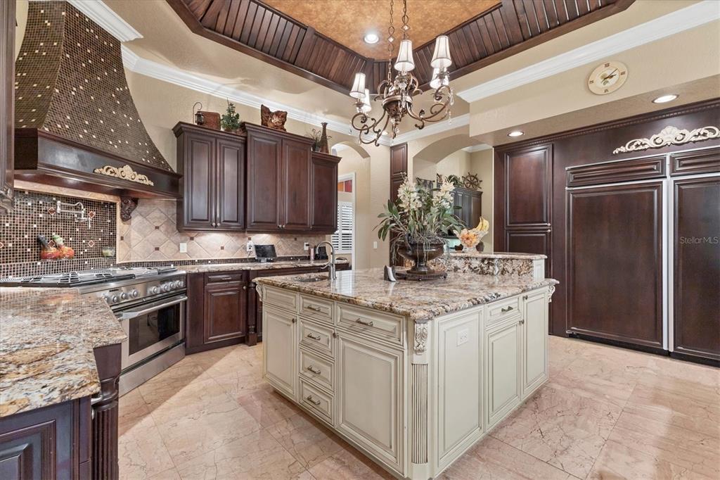A kitchen features dark wood cabinetry, a cream-colored island, granite countertops, and a chandelier — 3657 TROPICAIRE BOULEVARD, NORTH PORT, FL
