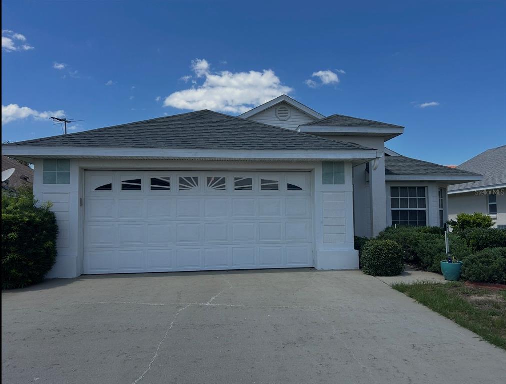 A single-story house with a white garage door, light-colored siding, and a gray shingled roof — 1030 CHALLENGER AVENUE, DAVENPORT, FL
