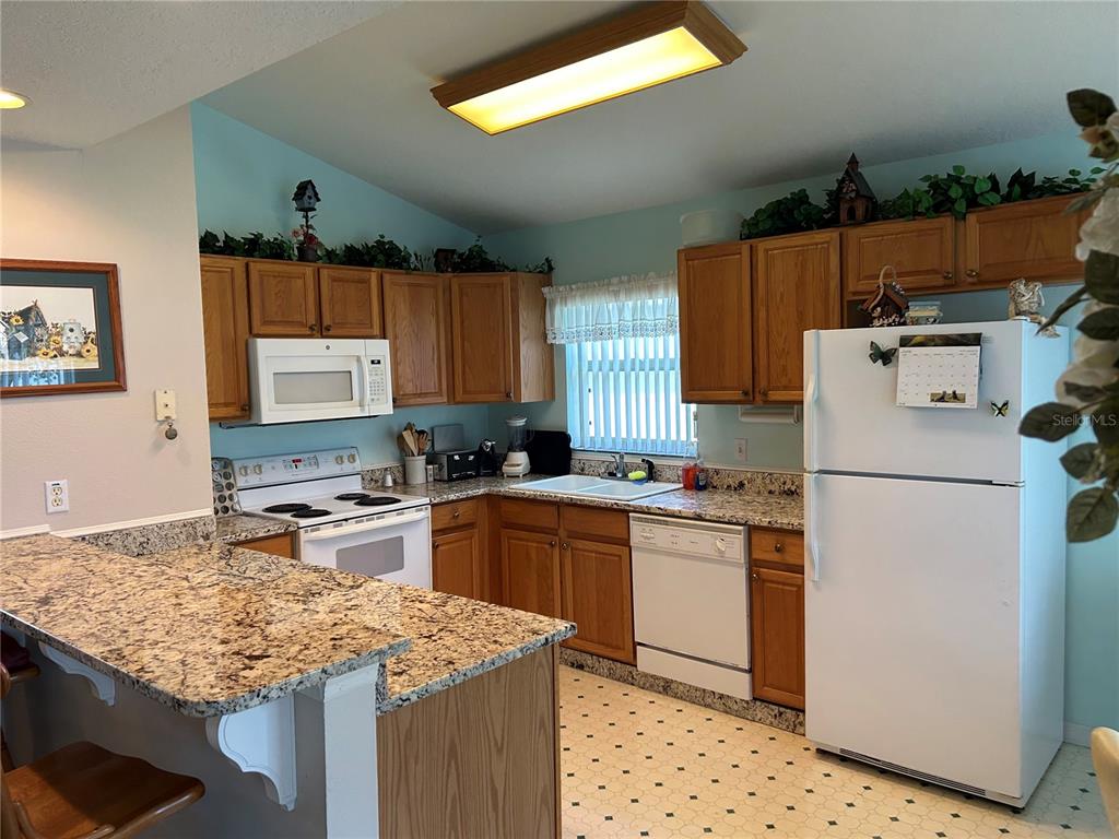 A kitchen features oak cabinets, granite countertops, white appliances, and a breakfast bar — 1030 CHALLENGER AVENUE, DAVENPORT, FL