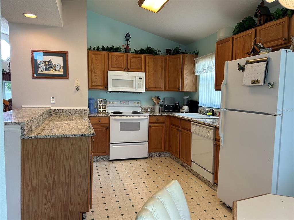 A kitchen features oak cabinets, white appliances, granite countertops, and a patterned vinyl floor — 1030 CHALLENGER AVENUE, DAVENPORT, FL