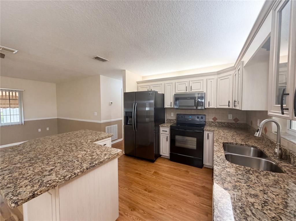 A kitchen features granite countertops, white cabinetry, stainless steel appliances, and wood-look flooring — 13763 SW 112TH TERRACE, DUNNELLON, FL