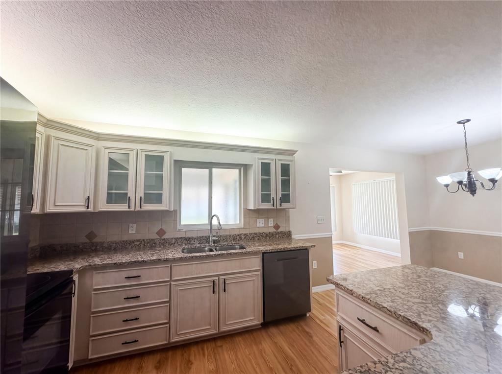A kitchen features light-colored cabinets, granite countertops, a stainless steel dishwasher, and wood flooring — 13763 SW 112TH TERRACE, DUNNELLON, FL