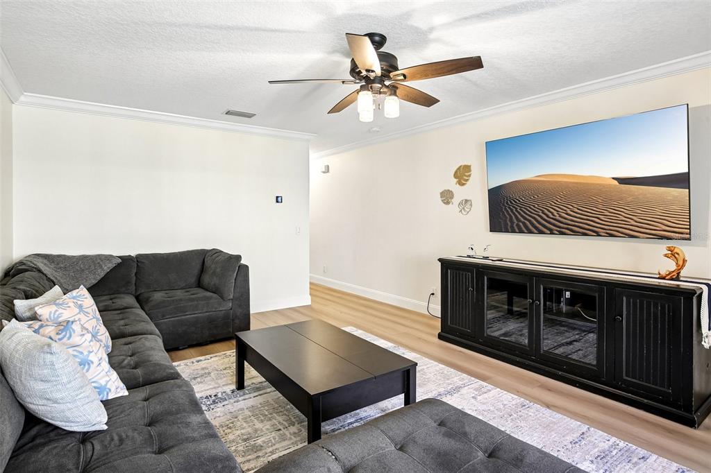 A living room features a gray sectional sofa, a black coffee table, and a wall-mounted television — 3853 ISLAND WAY, ST PETERSBURG, FL