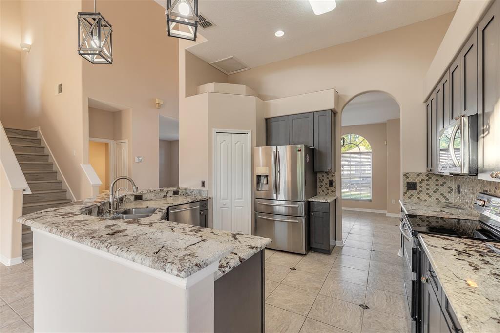 A kitchen with granite countertops, dark cabinets, stainless steel appliances, and a staircase nearby — 1424 NEW BOLTON DRIVE, PORT ORANGE, FL