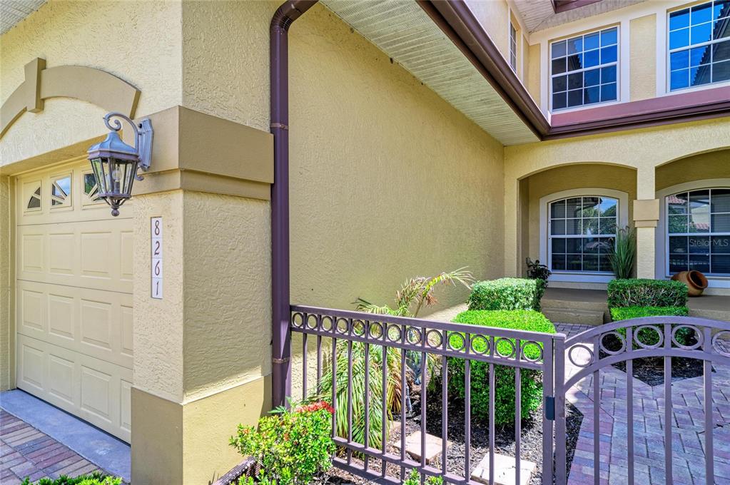 The exterior of a house features a garage, a gated entryway, and a paved walkway — 8261 MIRAMAR WAY UNIT 202, LAKEWOOD RANCH, FL