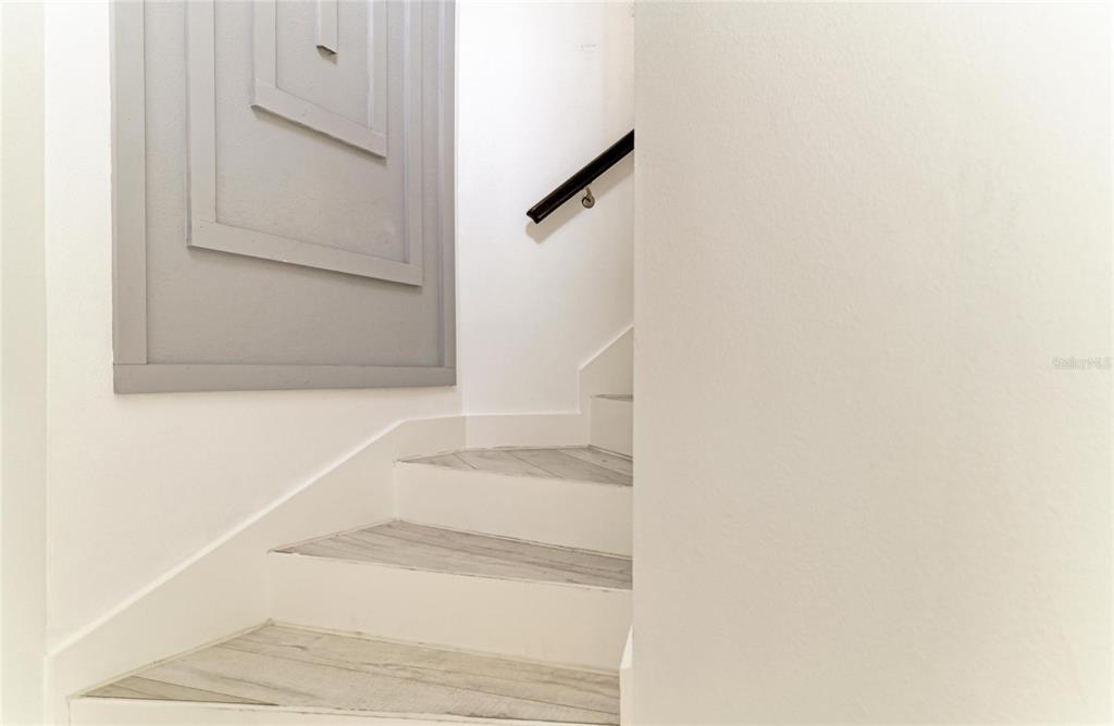 A staircase with light wood-look treads and a black handrail leads upward — 8261 MIRAMAR WAY UNIT 202, LAKEWOOD RANCH, FL