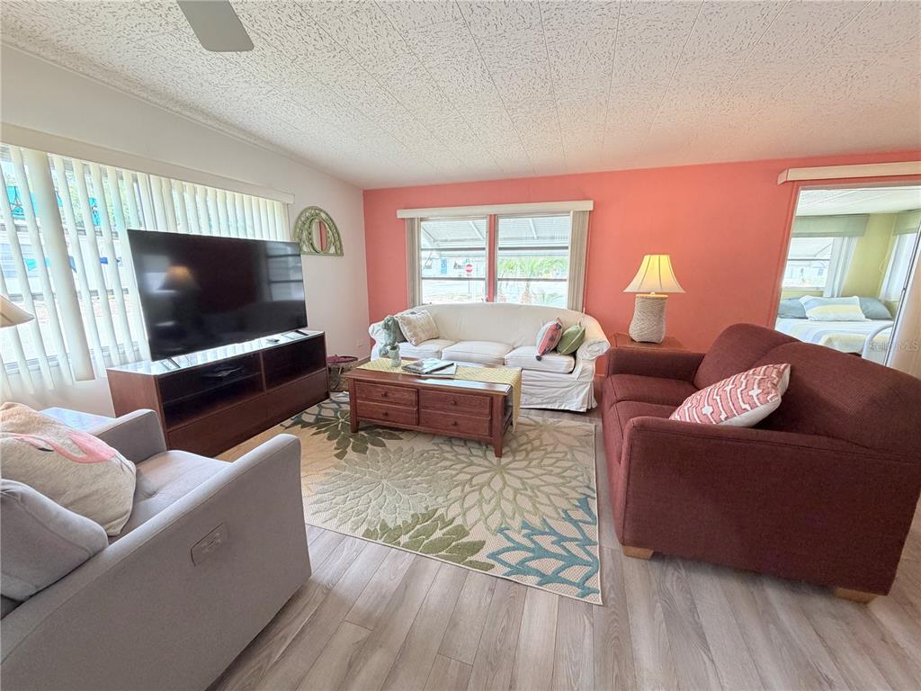 A living room features a coral accent wall, light wood flooring, and three pieces of furniture — 2331 BELLEAIR ROAD UNIT 529, CLEARWATER, FL