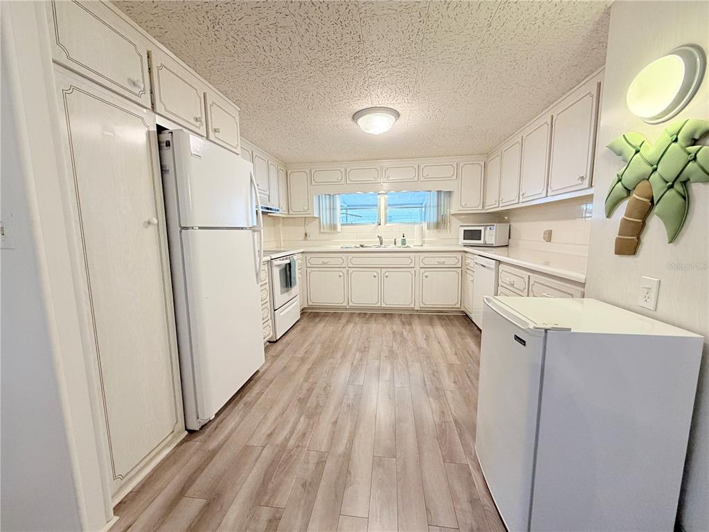 A kitchen features white cabinets, white appliances, and light wood-look flooring — 2331 BELLEAIR ROAD UNIT 529, CLEARWATER, FL