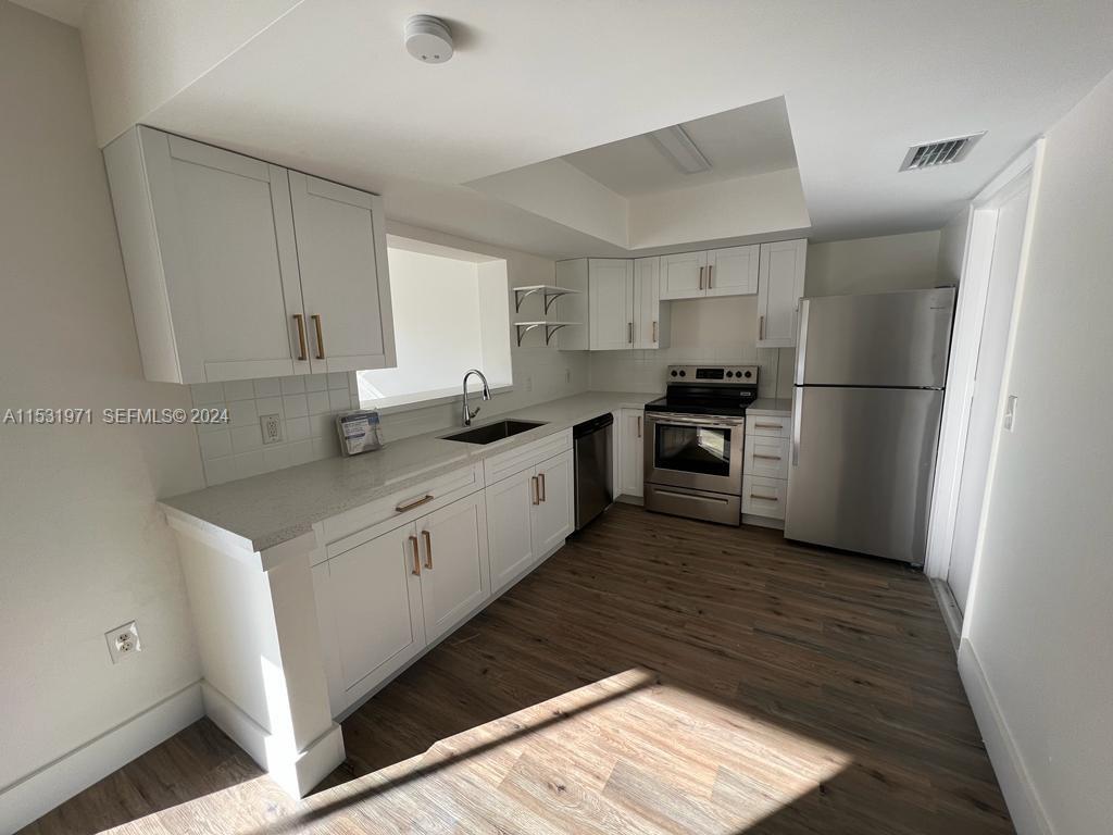 A kitchen features white cabinets, stainless steel appliances, and wood-look flooring — 11520 NW 31st Pl, Sunrise FL 33323, SUNRISE, FL