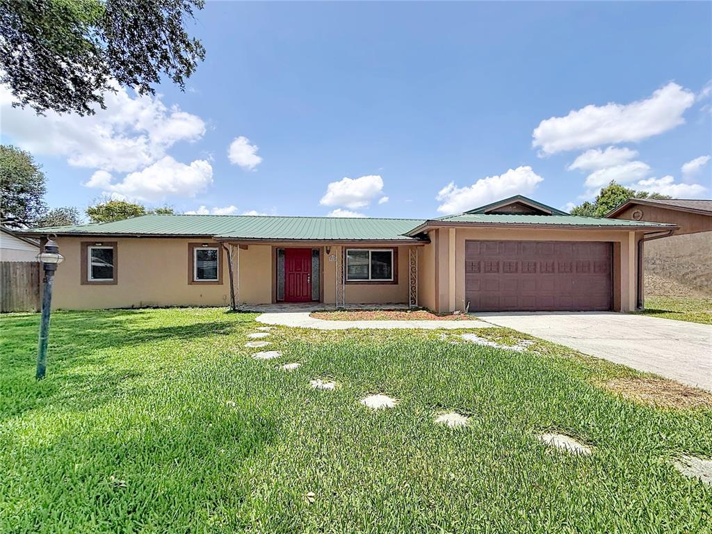 A single-story house with a green metal roof, tan stucco walls, and a red front door — 912 SHANGRI LA DRIVE, SEFFNER, FL