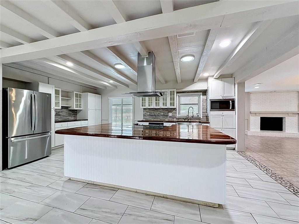 A kitchen features a large wooden island, white cabinetry, stainless steel appliances, and exposed ceiling beams — 912 SHANGRI LA DRIVE, SEFFNER, FL