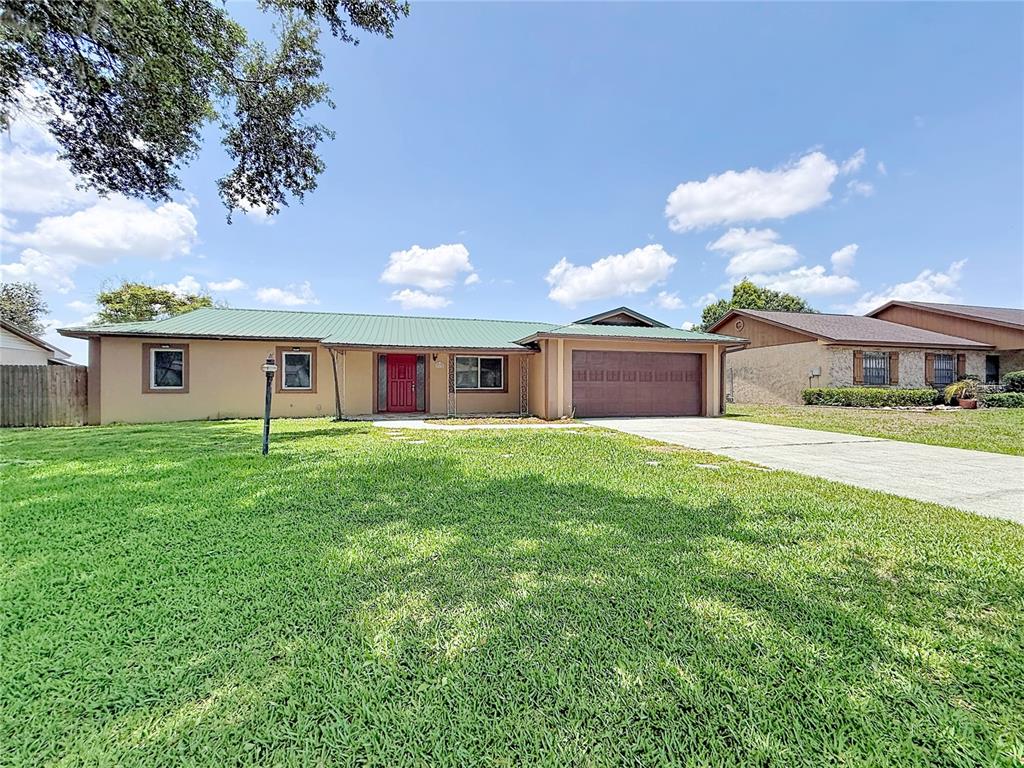 A single-story house with a green metal roof, tan stucco exterior, and attached garage — 912 SHANGRI LA DRIVE, SEFFNER, FL