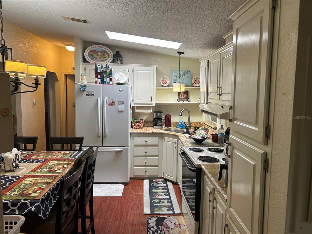 A kitchen features white cabinetry, a refrigerator, a dining table, and a sloped ceiling skylight — 731 POLO PARK EAST BOULEVARD, DAVENPORT, FL