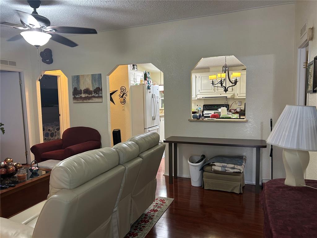 A living room with wood floors features a pass-through window looking into the kitchen — 731 POLO PARK EAST BOULEVARD, DAVENPORT, FL