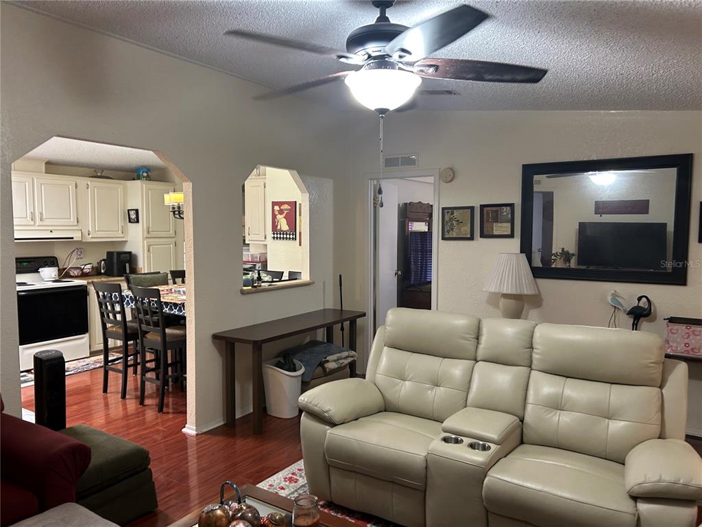 A living room with a light-colored leather sofa, ceiling fan, and an adjacent kitchen area — 731 POLO PARK EAST BOULEVARD, DAVENPORT, FL