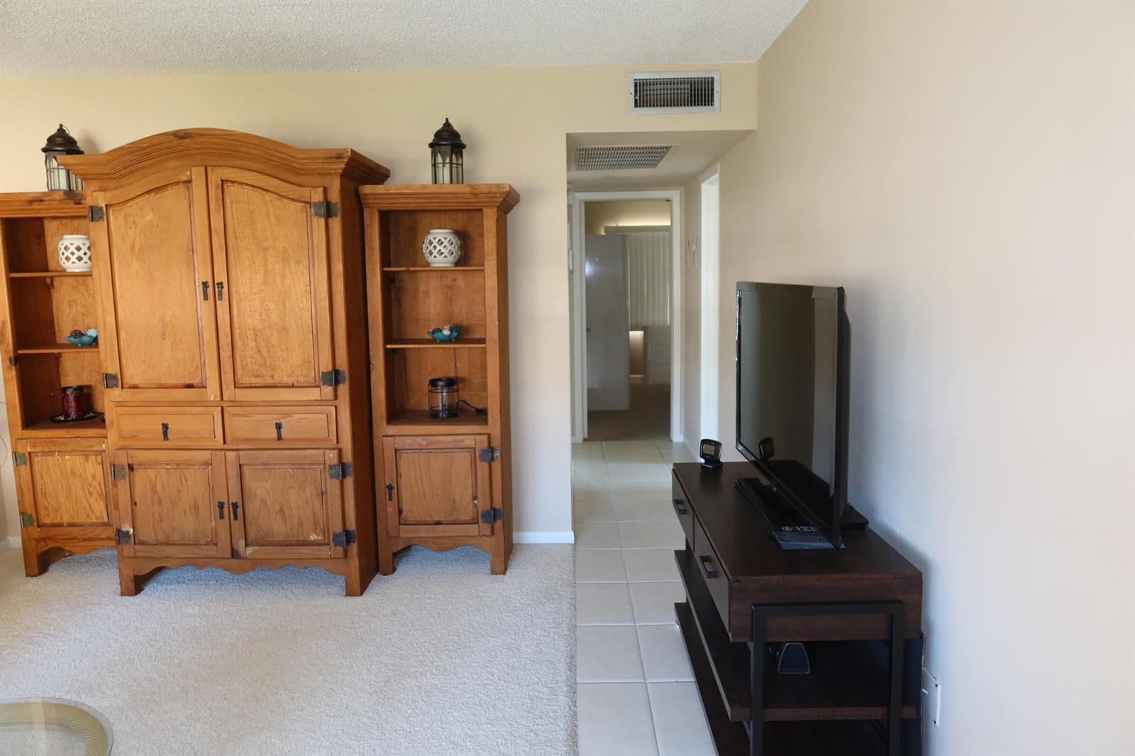 A living room features a large wooden entertainment center, a television stand, and a hallway — 102 Brighton C, Boca Raton FL 33434, BOCA RATON, FL