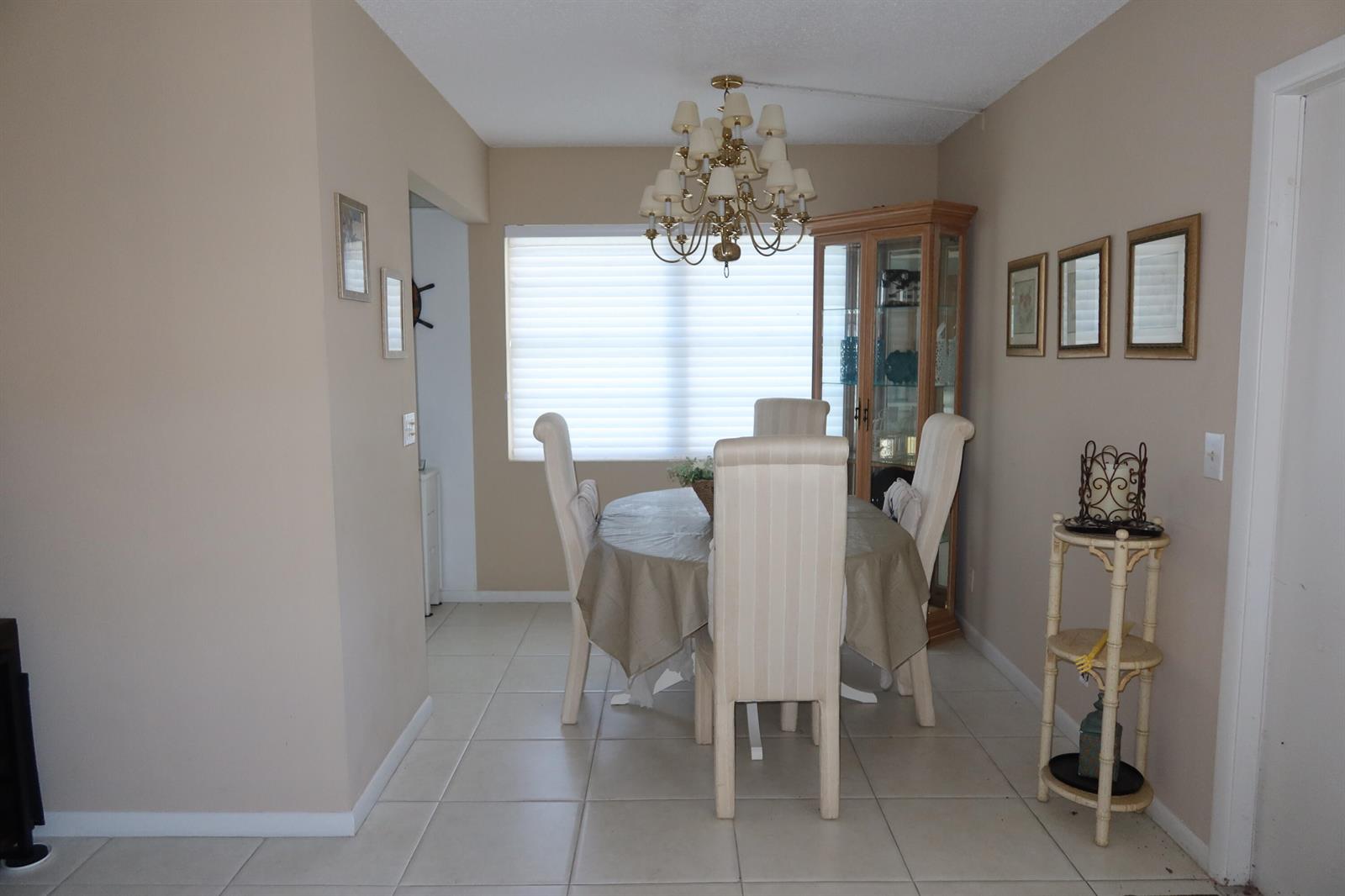 A dining room features a round table with chairs, a chandelier, and a wooden china cabinet — 102 Brighton C, Boca Raton FL 33434, BOCA RATON, FL