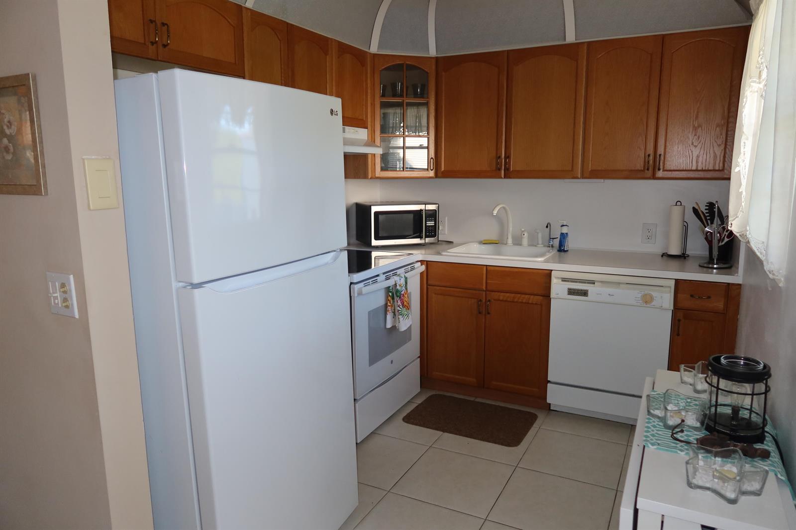 A kitchen features wood cabinets, white appliances, a white sink, and light-colored tile flooring — 102 Brighton C, Boca Raton FL 33434, BOCA RATON, FL