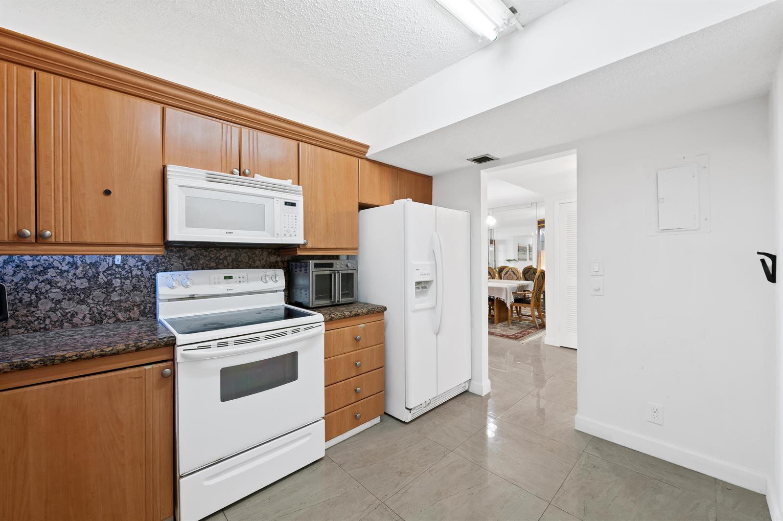 A kitchen features wood cabinets, granite countertops, white appliances, and tile flooring — 2500 Parkview Drive # 615, Hallandale Beach FL 33009, HALLANDALE BEACH, FL