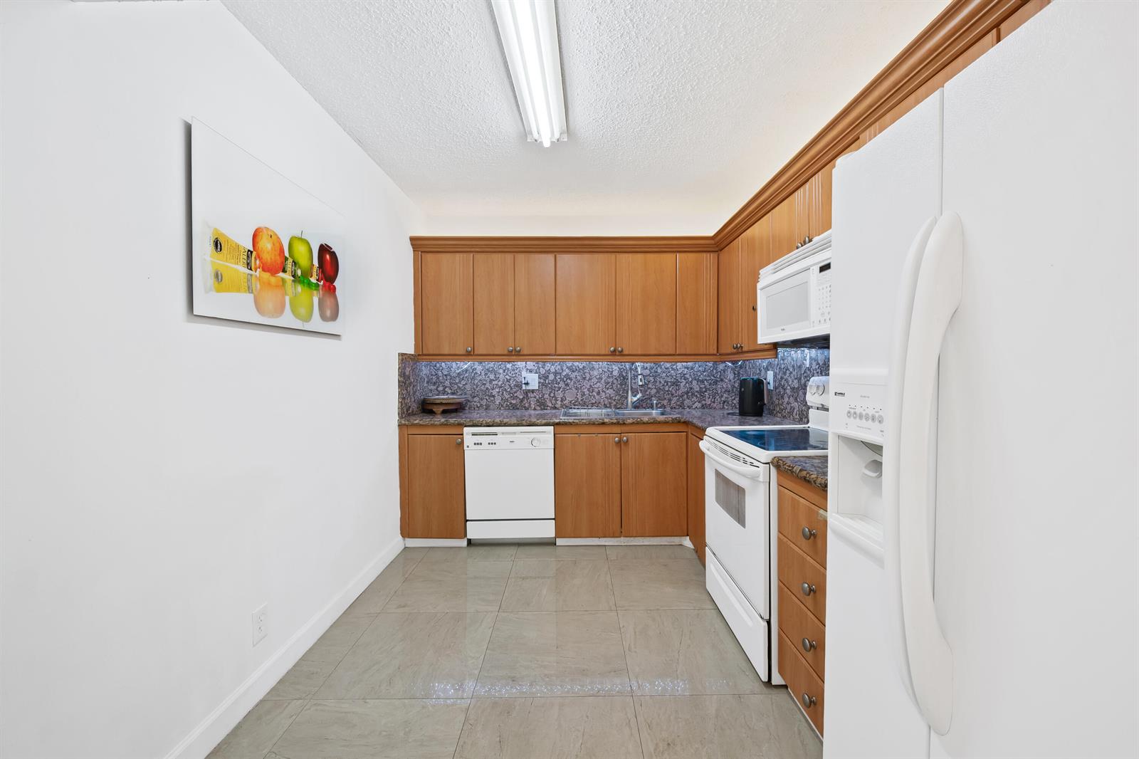 A kitchen features wood cabinets, granite countertops, white appliances, and light-colored tile flooring — 2500 Parkview Drive # 615, Hallandale Beach FL 33009, HALLANDALE BEACH, FL