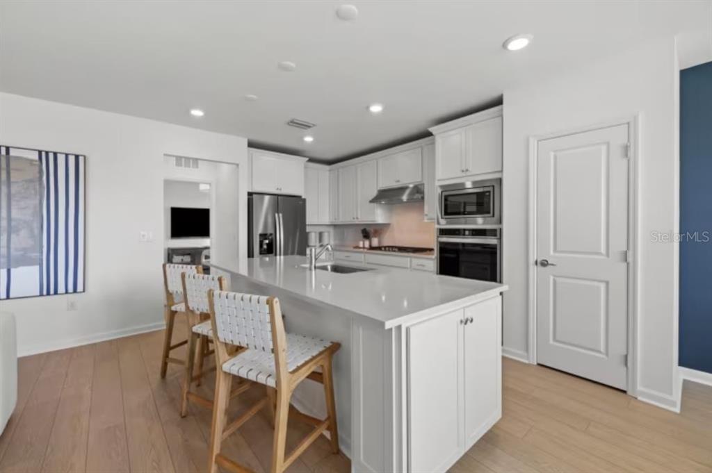 A modern kitchen features white cabinetry, a large central island with bar seating, and appliances — 3948 MARBURY COURT, DAVENPORT, FL