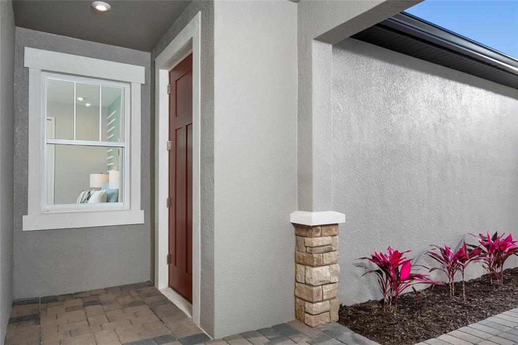 A red front door sits next to a window and a stone-accented pillar — 17768 STILLNESS COURT, VENICE, FL