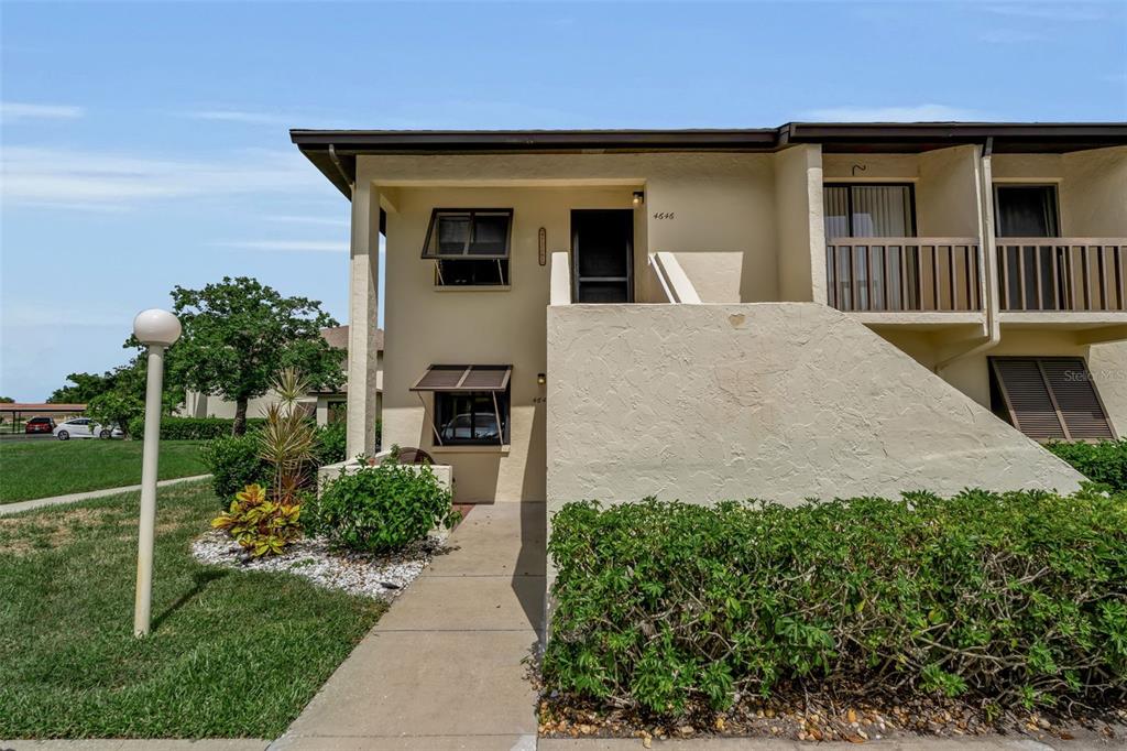 A two-story stucco apartment building features a concrete walkway leading to a covered entrance — 4644 LONGWATER CHASE UNIT 97, SARASOTA, FL