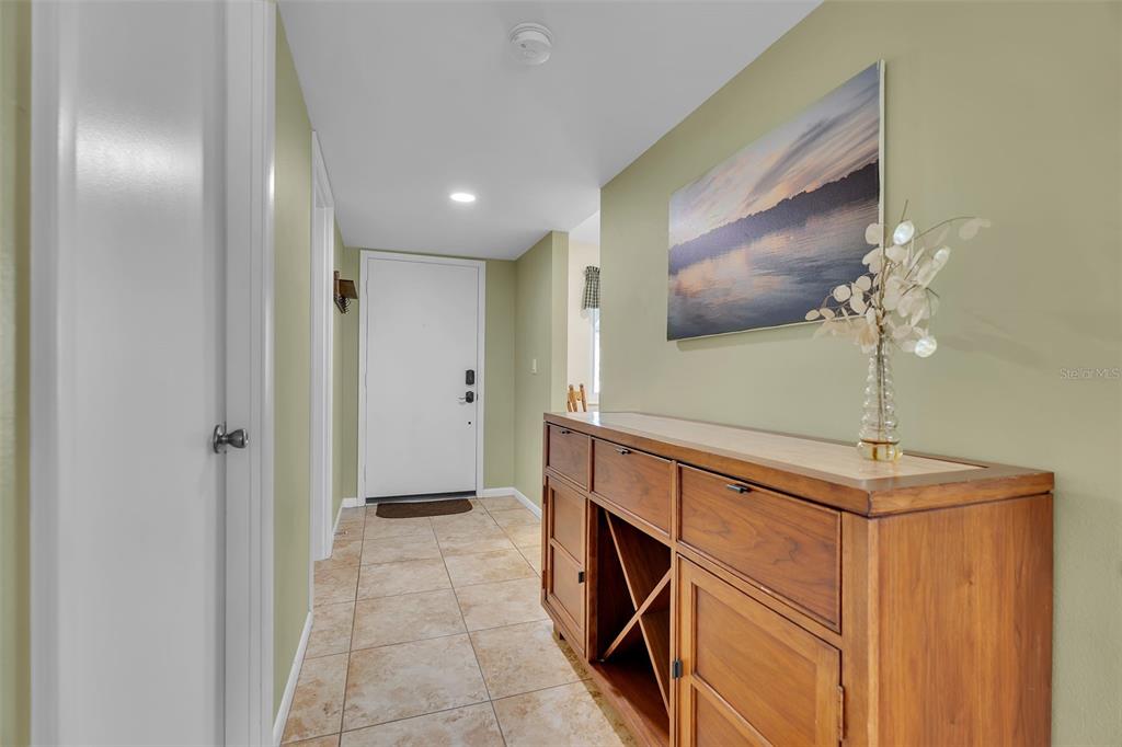 A tiled entryway features a wooden sideboard and a landscape painting on a green wall — 4644 LONGWATER CHASE UNIT 97, SARASOTA, FL
