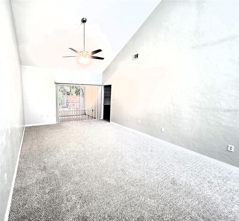 An empty living room with gray carpet, vaulted ceilings, a ceiling fan, and sliding glass doors — 13200 W NEWBERRY ROAD UNIT BB155, NEWBERRY, FL