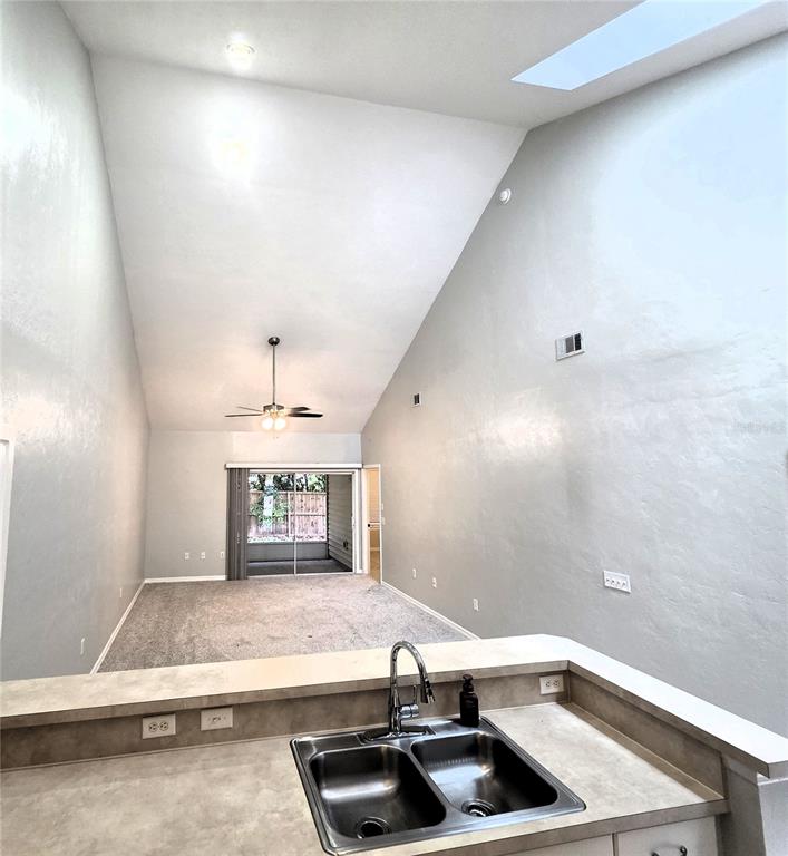 A kitchen sink overlooks a living area with vaulted ceilings, carpeted floors, and sliding doors — 13200 W NEWBERRY ROAD UNIT BB155, NEWBERRY, FL