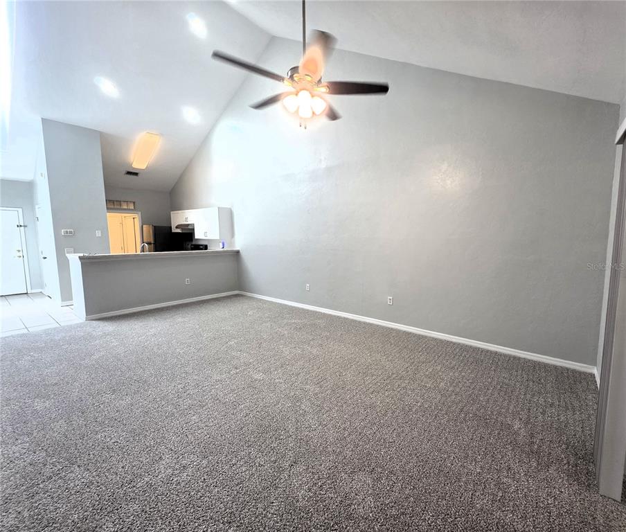 A living room with gray carpet, a vaulted ceiling, a ceiling fan, and a kitchen pass-through — 13200 W NEWBERRY ROAD UNIT BB155, NEWBERRY, FL
