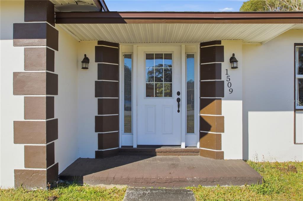 The exterior front entrance features a white door with sidelights and brown decorative corner blocks — 1509 GOLD TERRACE, DELTONA, FL