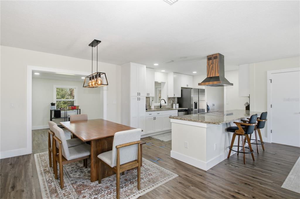 A dining area and kitchen feature white cabinetry, a wooden range hood, and granite countertops — 1509 GOLD TERRACE, DELTONA, FL