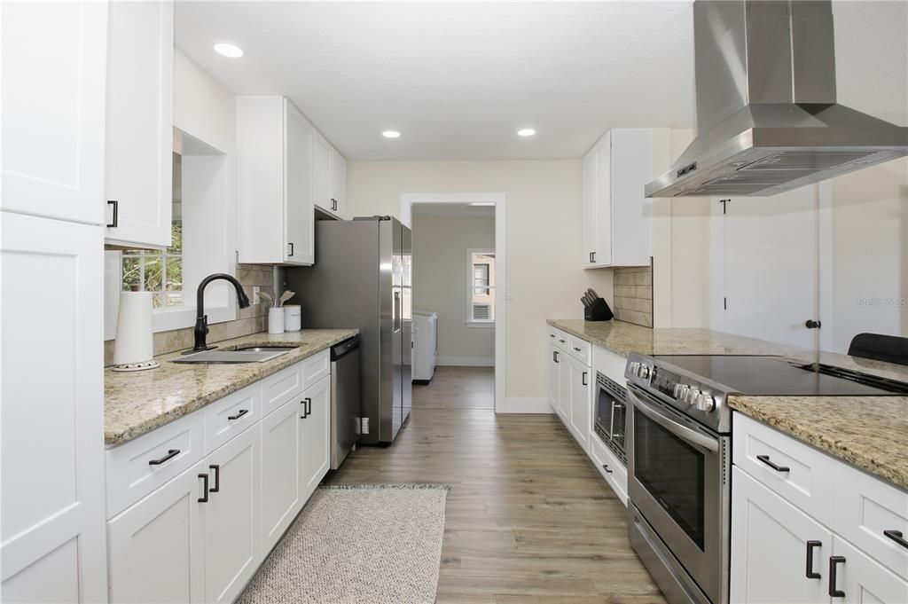 A kitchen features white cabinets, granite countertops, stainless steel appliances, and wood-look flooring — 1509 GOLD TERRACE, DELTONA, FL