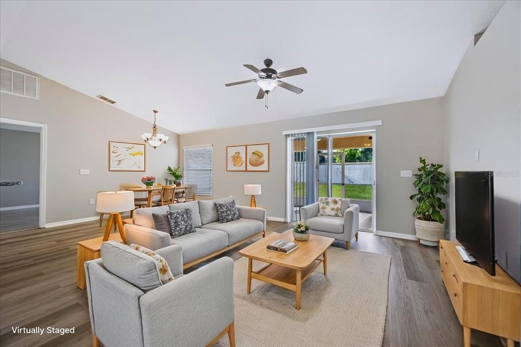 A living room with light gray walls, wood-look flooring, a ceiling fan, and sliding glass doors — 8810 PEBBLEBROOKE DRIVE, LAKELAND, FL