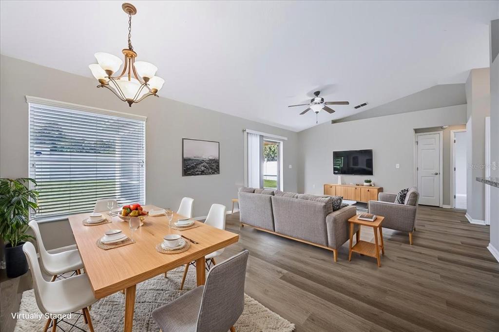 A living and dining area featuring light wood flooring, neutral walls, and a vaulted ceiling — 8810 PEBBLEBROOKE DRIVE, LAKELAND, FL