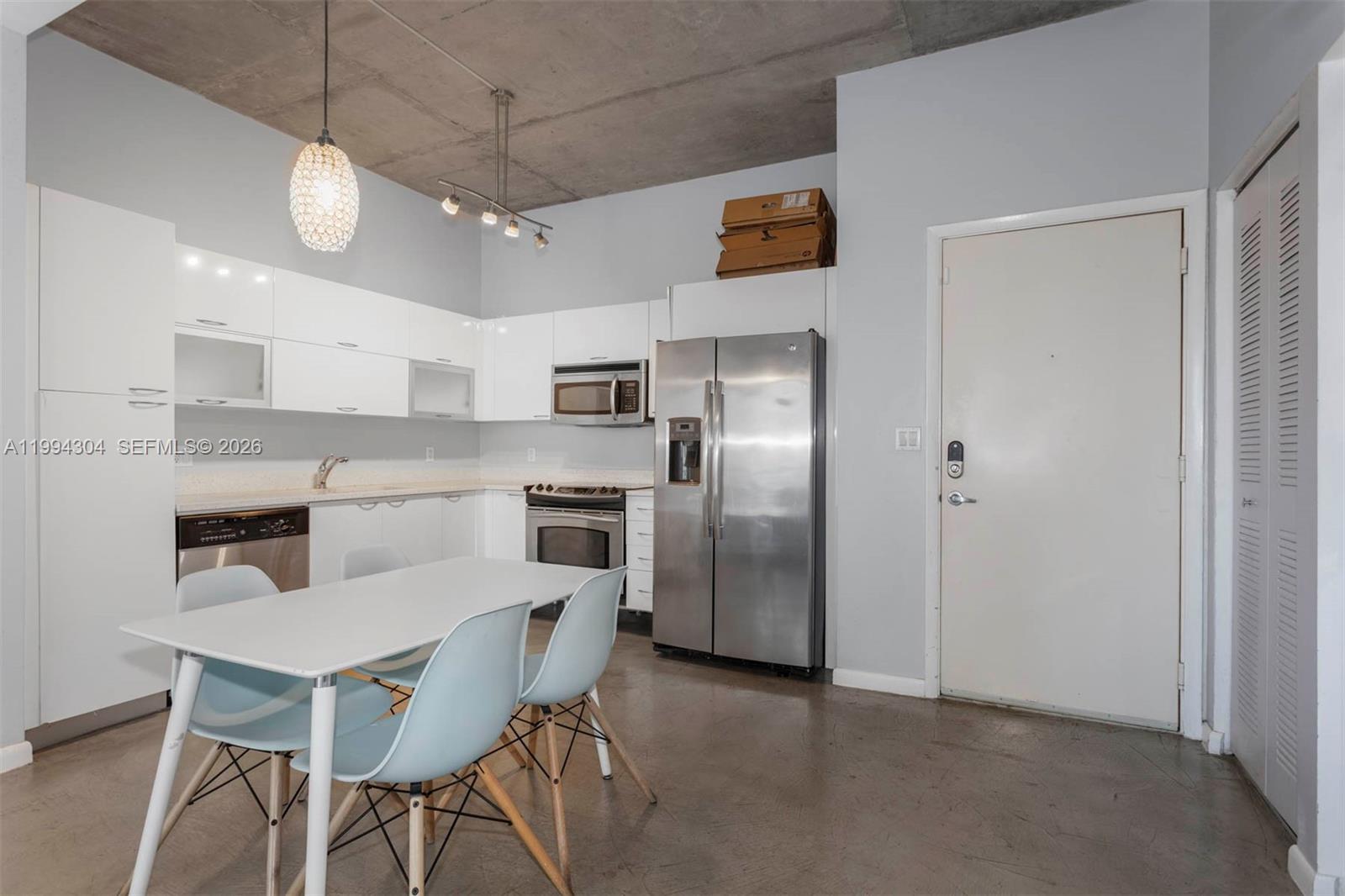 A kitchen with white cabinets, stainless steel appliances, and a dining table on concrete floors — 234 NE 3rd St # 1106, Miami FL 33132, MIAMI, FL