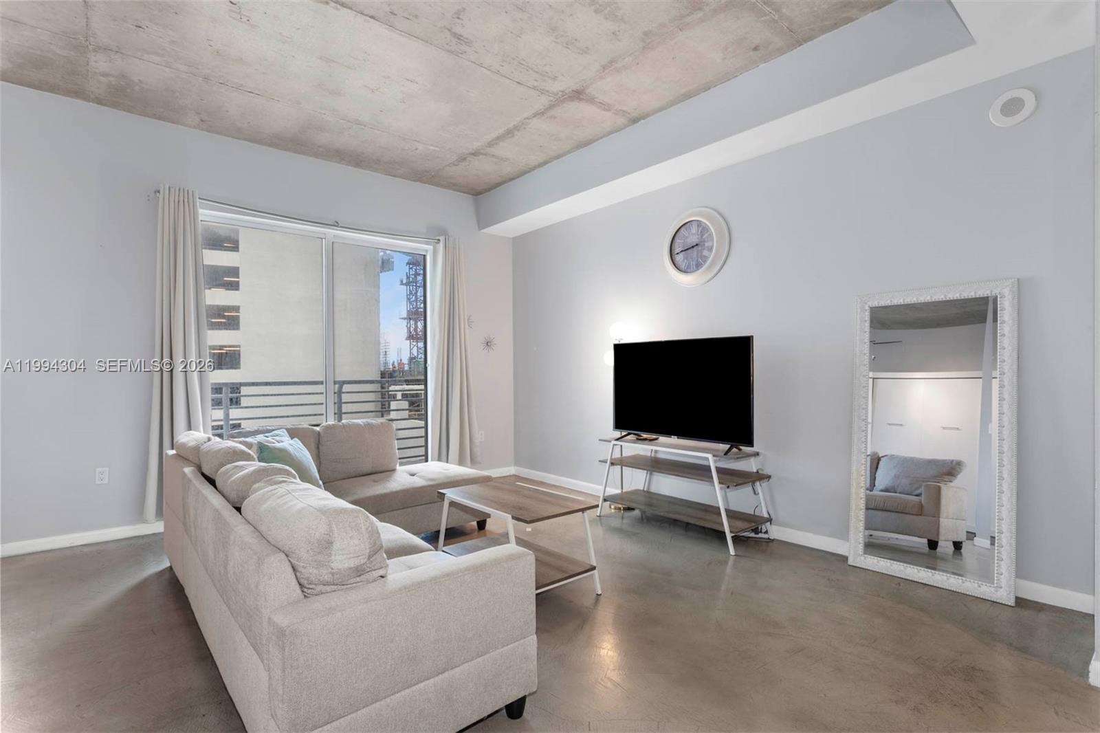 A living room features a concrete ceiling, light gray walls, a sectional sofa, and a balcony — 234 NE 3rd St # 1106, Miami FL 33132, MIAMI, FL