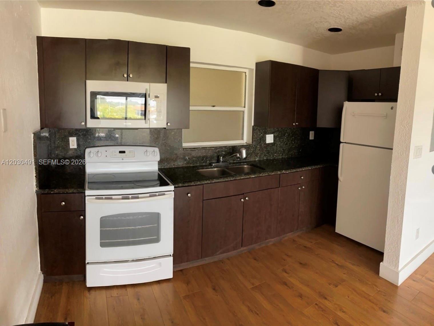 A kitchen features dark wood cabinets, granite countertops, white appliances, and wood-look flooring — 7410 SW 82nd St # K401, Miami FL 33143, MIAMI, FL