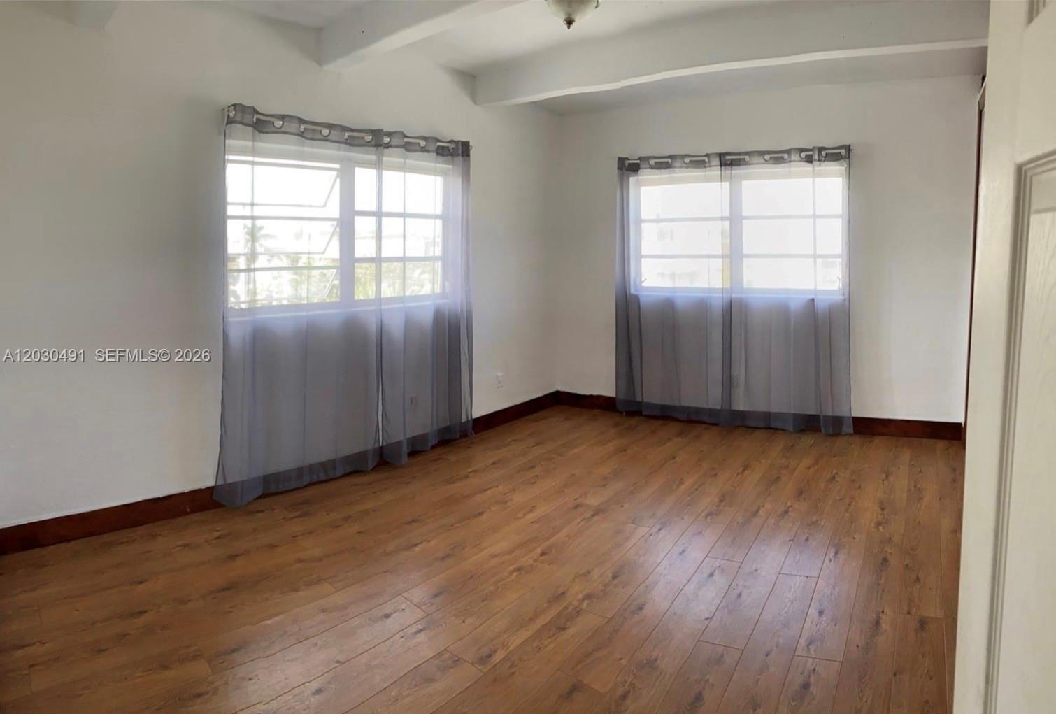 An empty bedroom features wood-look flooring, white walls, and two windows with sheer curtains — 7410 SW 82nd St # K401, Miami FL 33143, MIAMI, FL