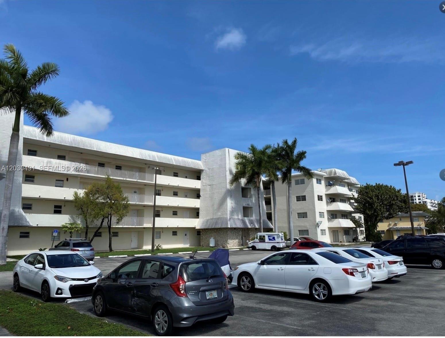 A multi-story apartment building with a parking lot in the foreground under a blue sky — 7410 SW 82nd St # K401, Miami FL 33143, MIAMI, FL