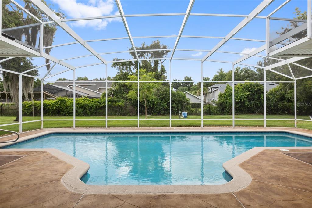 A screened-in swimming pool with a concrete deck overlooks a grassy backyard and trees — 15900 ACORN CIRCLE, TAVARES, FL
