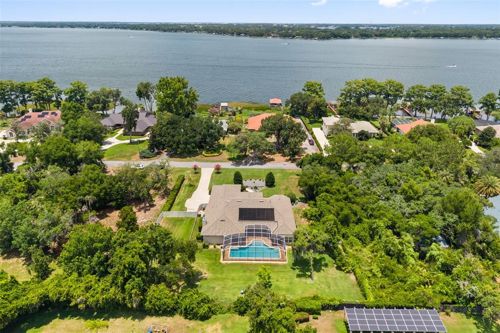 An aerial view shows a house with a pool and solar panels near a lake — 15900 ACORN CIRCLE, TAVARES, FL