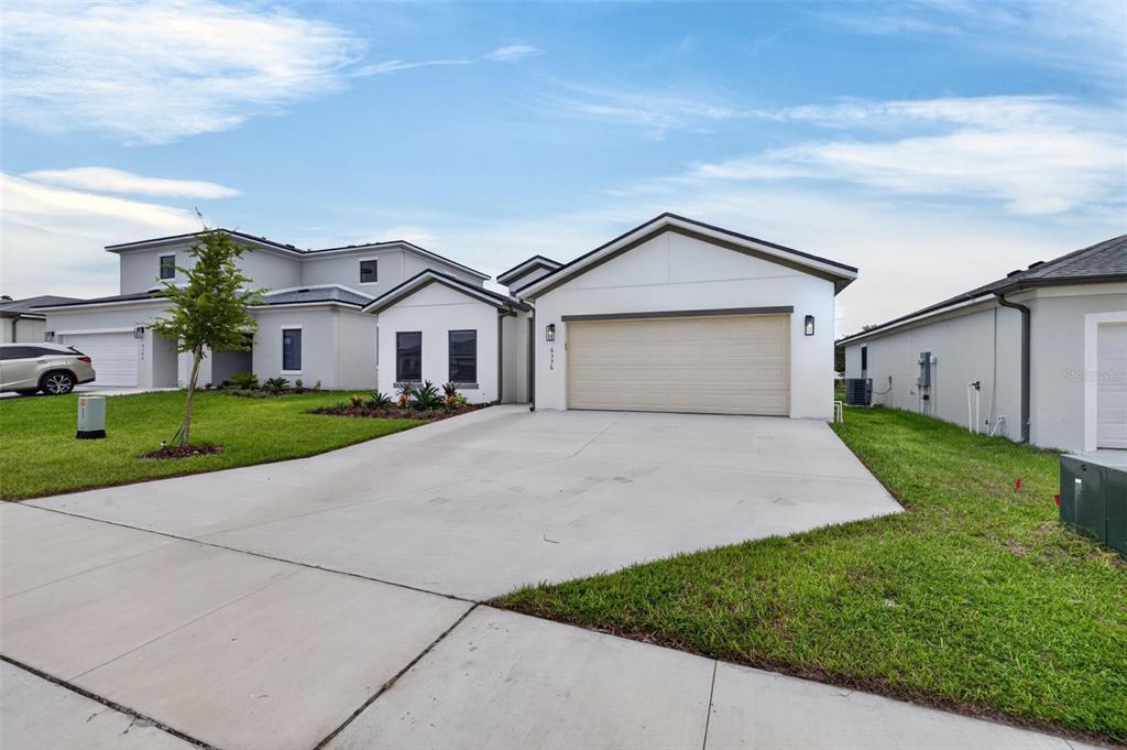A modern, single-story house with a beige garage door and a concrete driveway — 6336 CHORUS DRIVE, MASCOTTE, FL