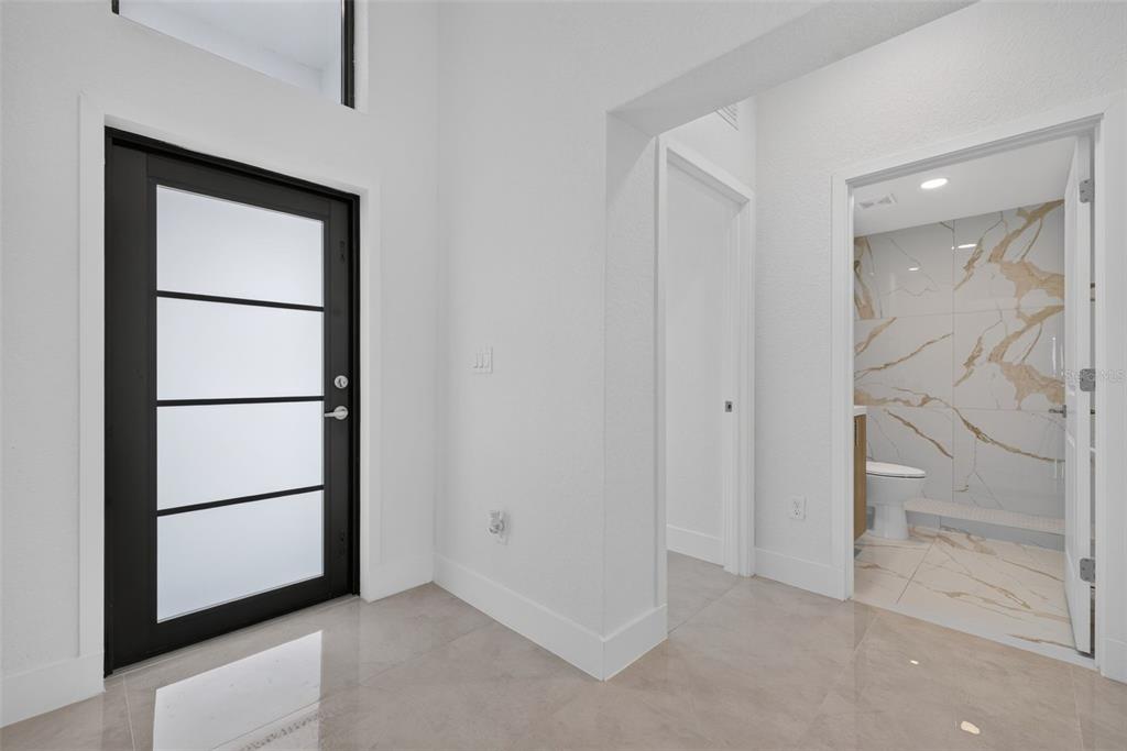 An entryway with a modern black-framed glass door leads to a tiled bathroom with marble-look walls — 6336 CHORUS DRIVE, MASCOTTE, FL
