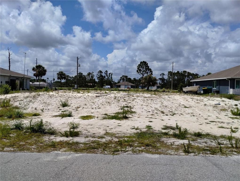 A vacant, sandy residential lot sits between two houses under a cloudy blue sky — 11320 POPLIN AVENUE, ENGLEWOOD, FL