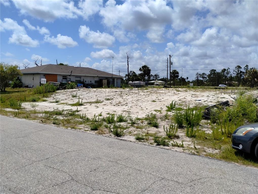 A vacant, sandy residential lot sits next to a single-story house under a cloudy sky — 11320 POPLIN AVENUE, ENGLEWOOD, FL